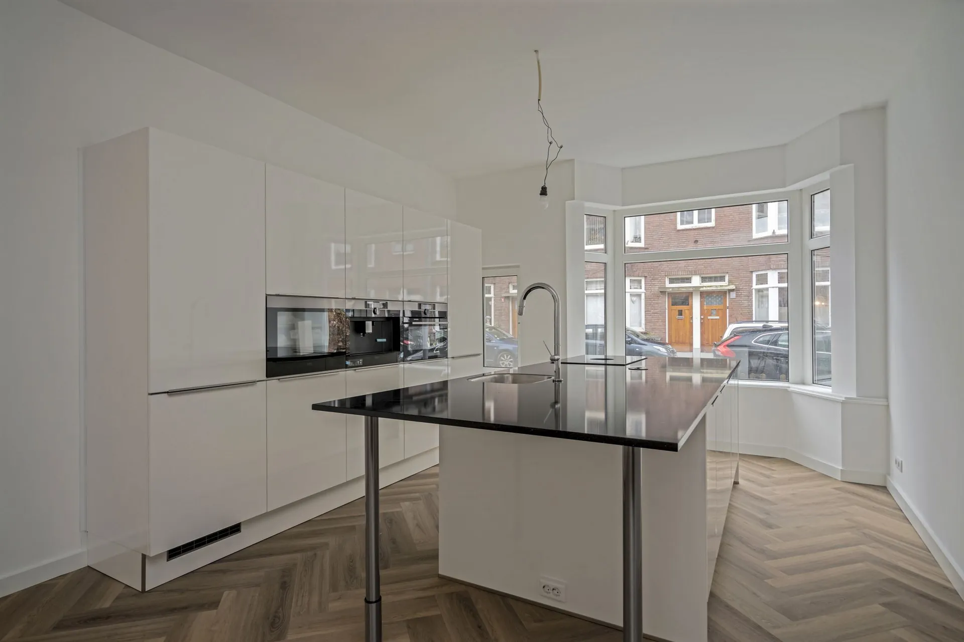 Gerenoveerde woning in Rotterdam: witte keuken met kookeiland en een visgraatvloer