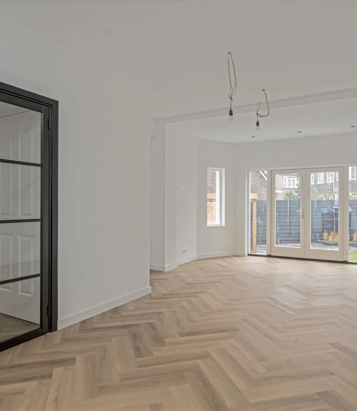Lichte woonkamer in Rotterdam met een zwarte stalen glazen deur en een visgraatvloer